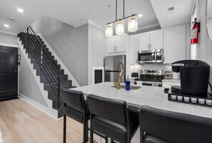 Une cuisine moderne avec un plan de travail en marbre, des chaises noires, des appareils électroménagers en acier inoxydable et un escalier noir.
