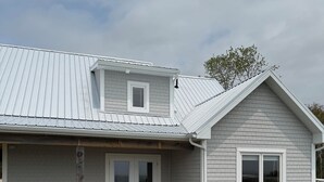 Ein zweigeschossiges Haus mit überdachter Terrasse, einer kleinen Holzterrasse und einem Rasen.