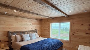 Ein Schlafzimmer einer Holzhütte mit einem Bett, einem Fenster und einem Nachttisch aus Holz.