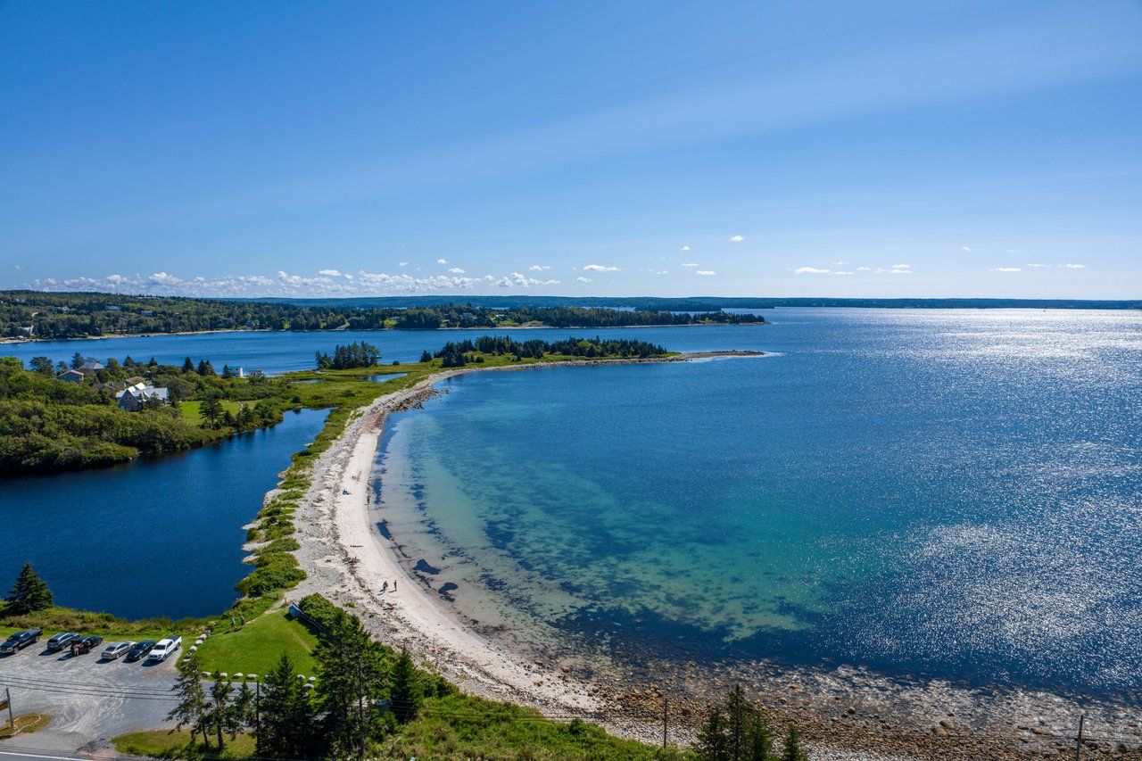 A coastal landscape with a clear beach, a parking area, and a road leading to the shore.