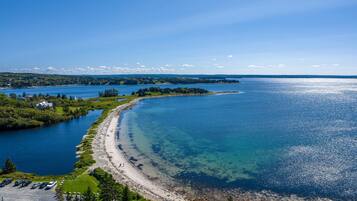 A coastal landscape with a clear beach, a parking area, and a road leading to the shore.