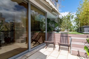 A patio with two wicker chairs, a glass door, and a view of a garden with various plants. - AGORA LOFT Acropolis View (Athens)