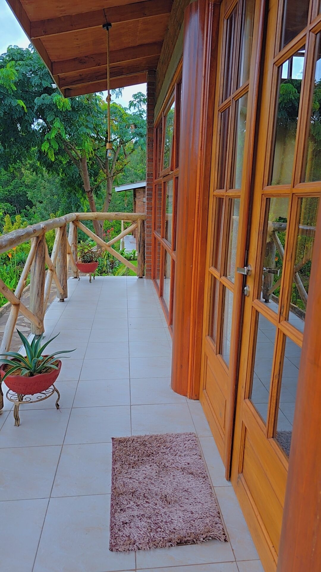 A wooden balcony with a tiled floor, potted plants, and a wooden railing.