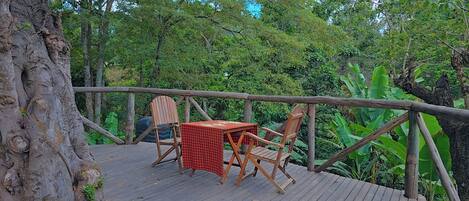 A wooden deck with a table and chairs, surrounded by dense greenery and trees.
