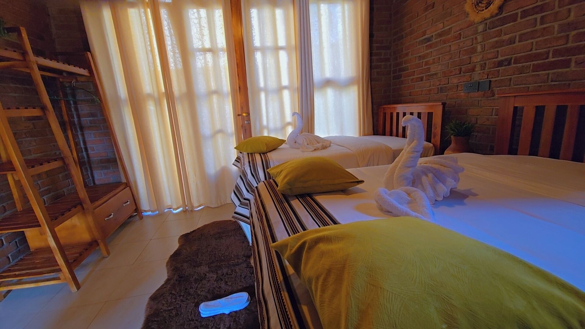 Habitación de hotel con pared de ladrillo, escalera de madera, cama con ropa de cama a rayas y toalla con forma de cisne.