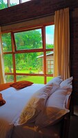 Una habitación con una cama, un ventanal con cortinas y vistas a un jardín.