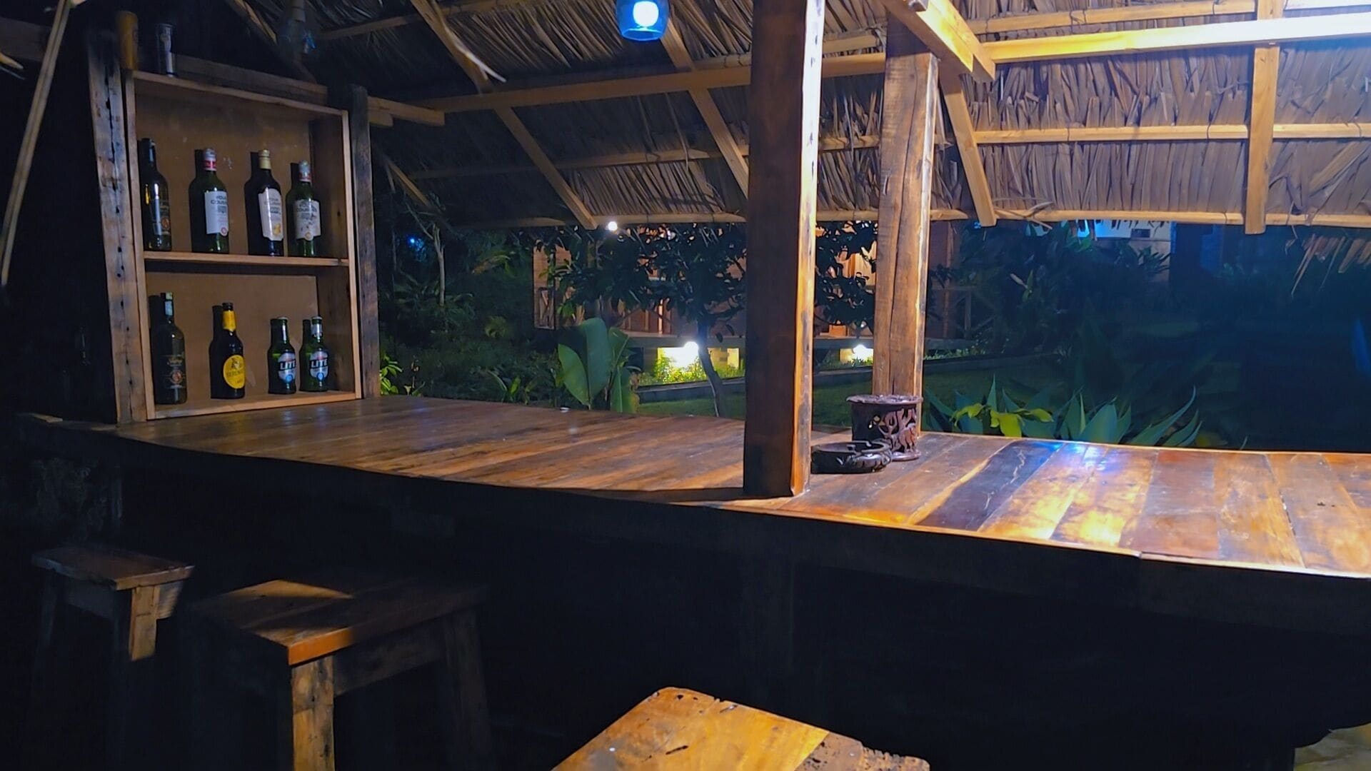 An outdoor bar area with wooden furniture and shelves stocked with bottles.