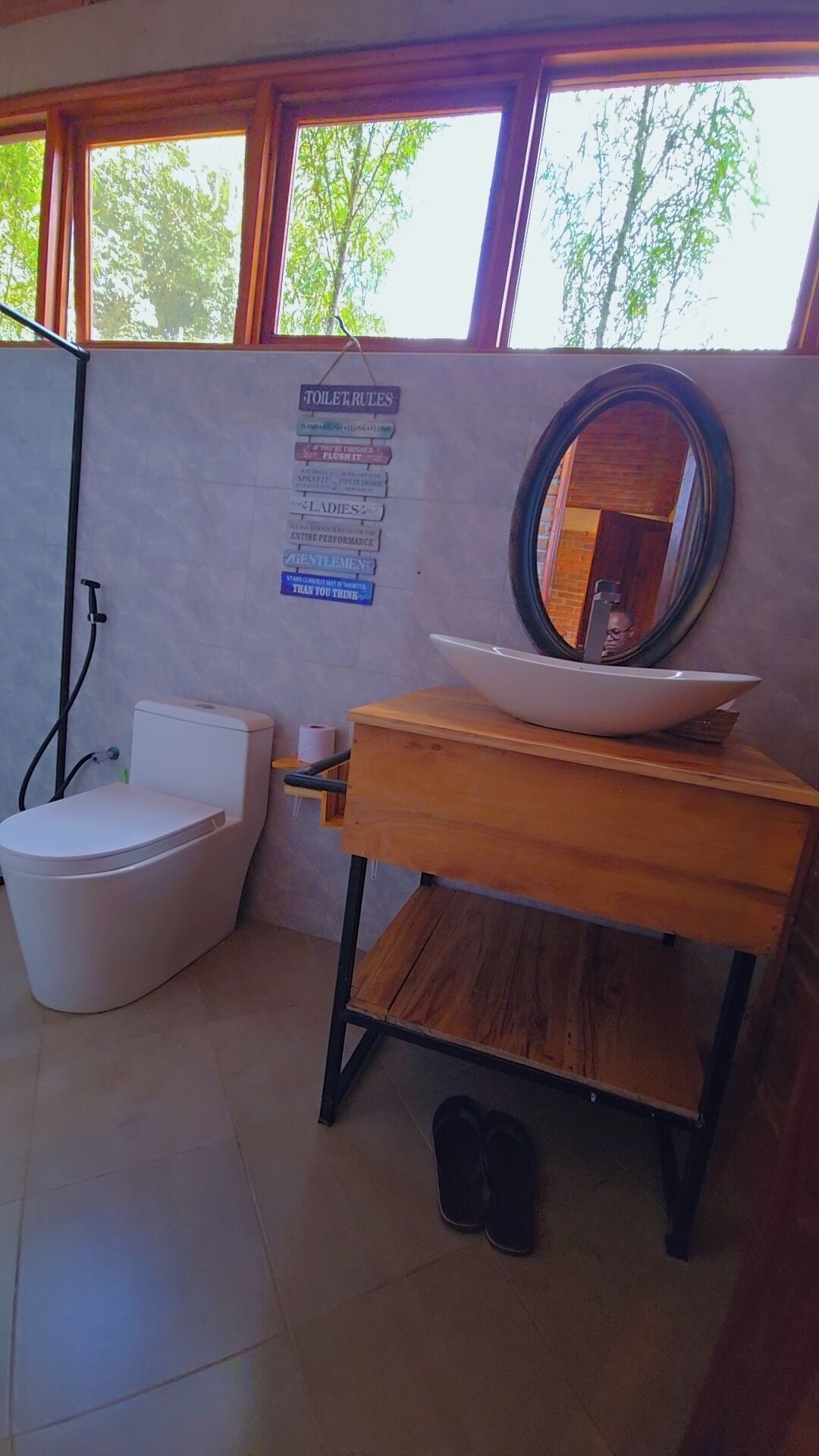Een badkamer met toilet, bidet en wastafel met spiegel. Er hangt een bord aan de muur met regels.
