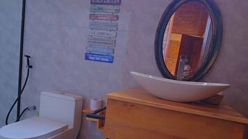 Een badkamer met toilet, bidet en wastafel met spiegel. Er hangt een bord aan de muur met regels.