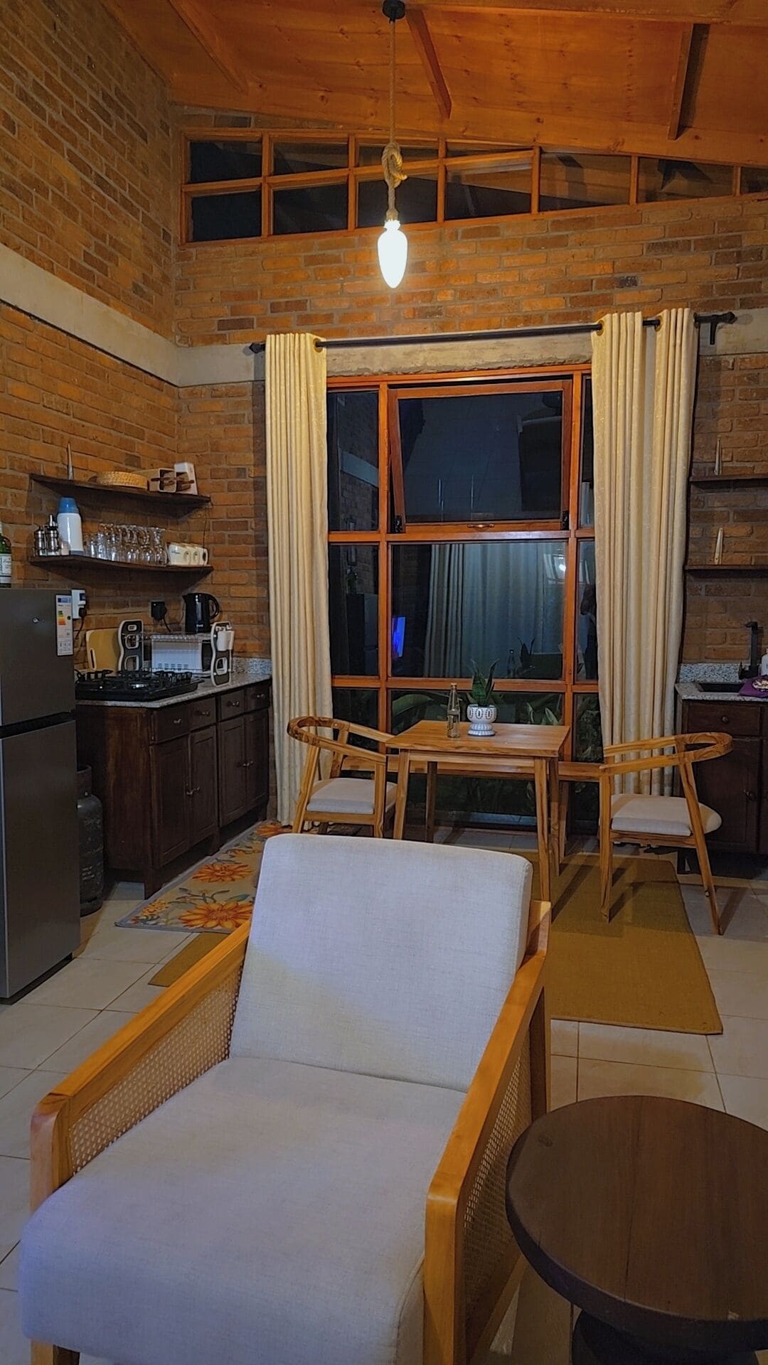 Un interior acollidor amb zona de menjador, cuina i un gran finestral amb cortines.