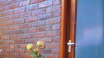 A wooden side table with a vase of yellow flowers, a wooden chair, and a brick wall.
