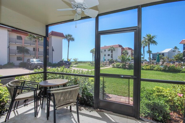 A balcony with wicker furniture, a ceiling fan, and a view of a well-maintained lawn and buildings. - Enjoy ocean views in this spacious 2BR condo on Sanibel Island Sandalfoot 4D1 (Sanibel Island)