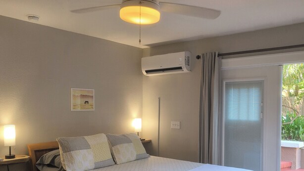 Un dormitorio con cama, lámparas de noche, aire acondicionado, ventilador de techo y vistas al exterior.