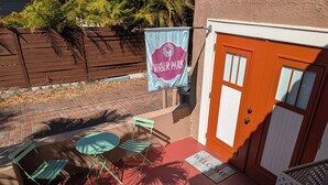 Un patio con una mesa y sillas, una puerta con un felpudo que dice 'WELCOME' y una pancarta colgada en una cerca.