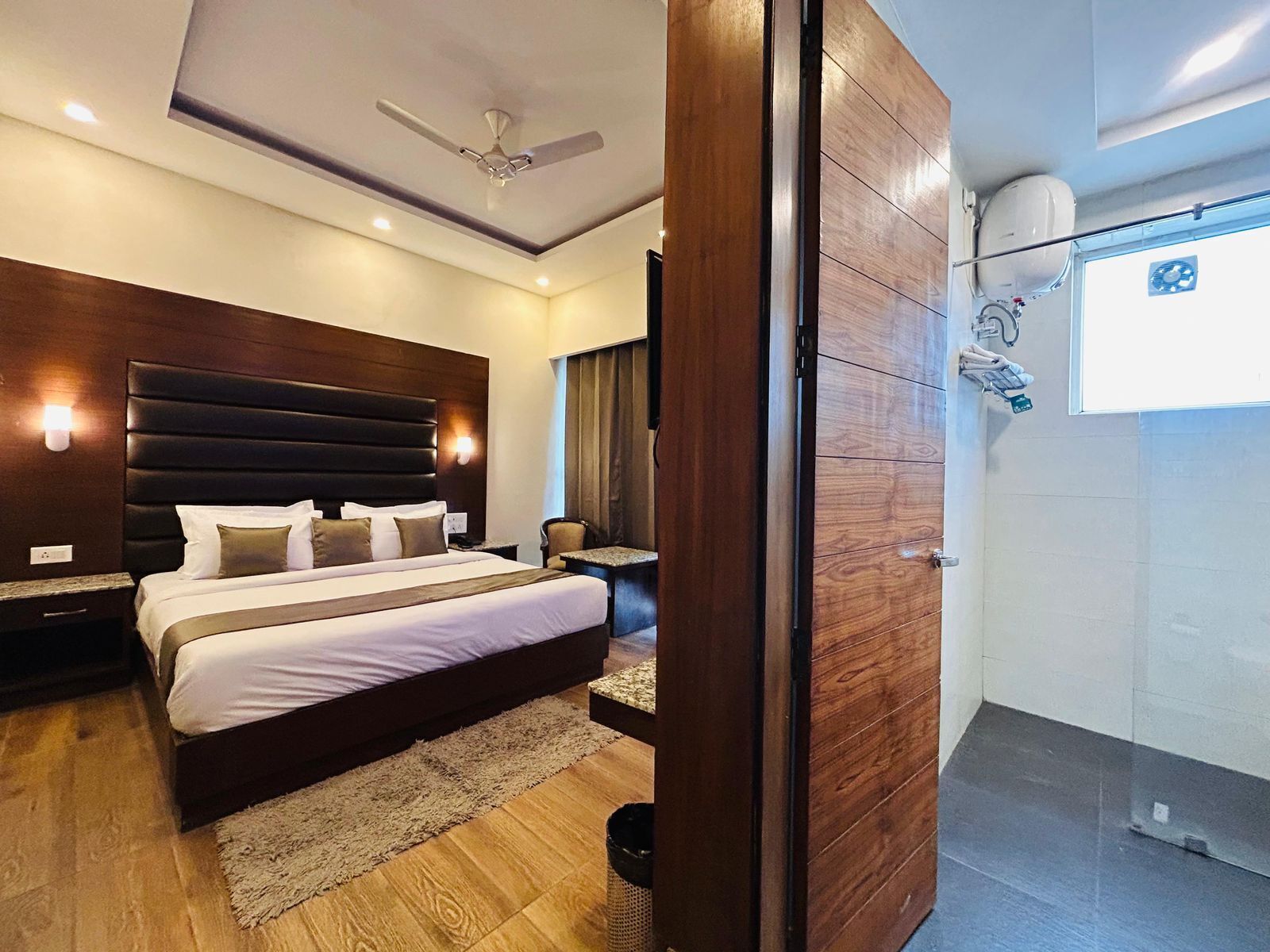 A modern hotel room with a large bed, a ceiling fan, and a view of the outside.