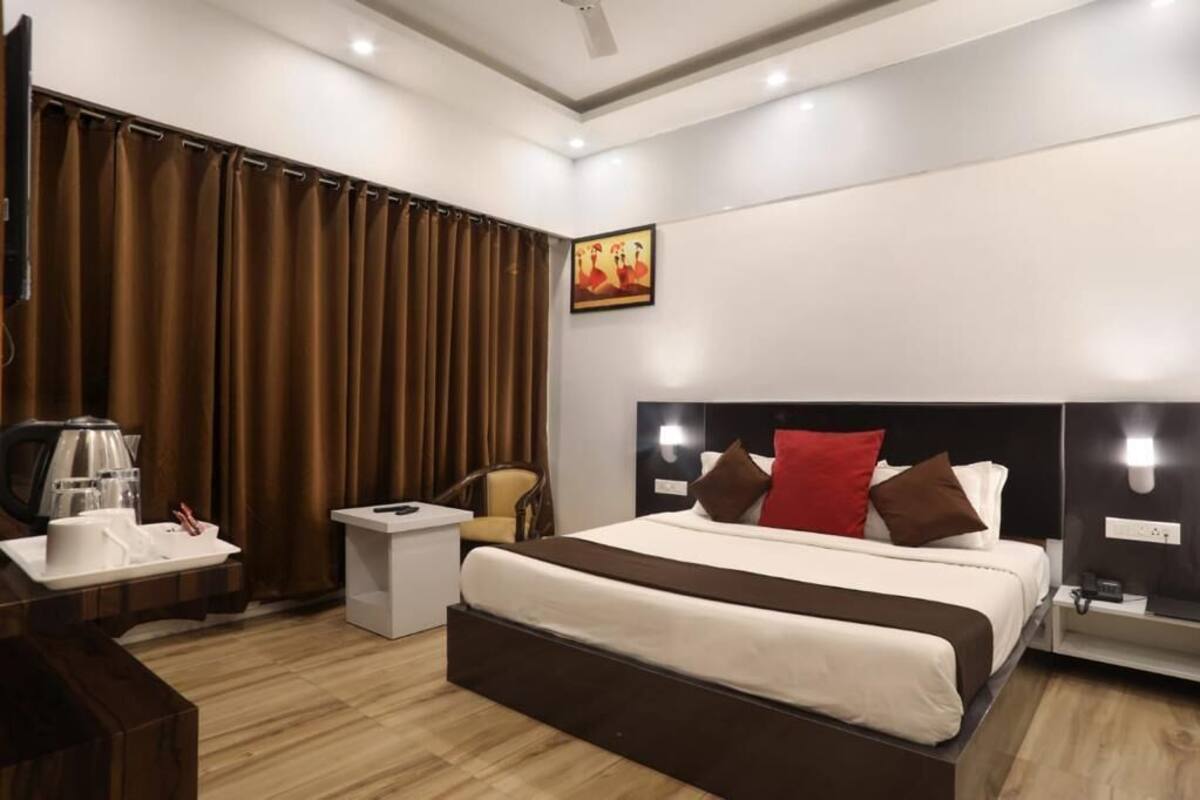 A hotel room with a bed, bedside tables, a chair, curtains, a painting, and a coffee maker.