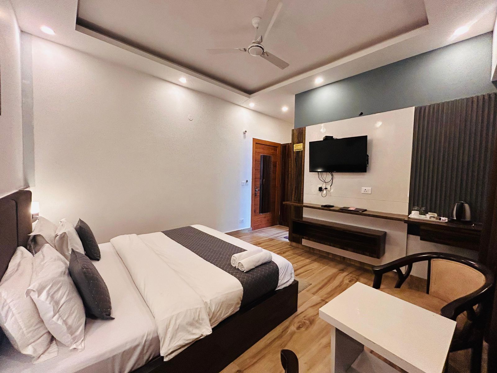 Habitación de hotel con cama, escritorio, silla, televisión y ventilador de techo.
