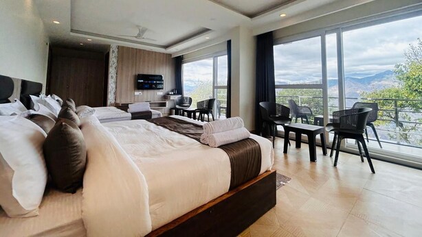 A modern bedroom with a large bed, a TV, a desk, and a balcony with a view.