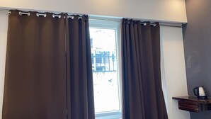 A window with brown curtains, a view of a balcony, and a small shelf with a kettle.