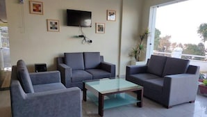 A living room with a sofa set, a coffee table, a TV mounted on the wall, and a balcony with potted plants.