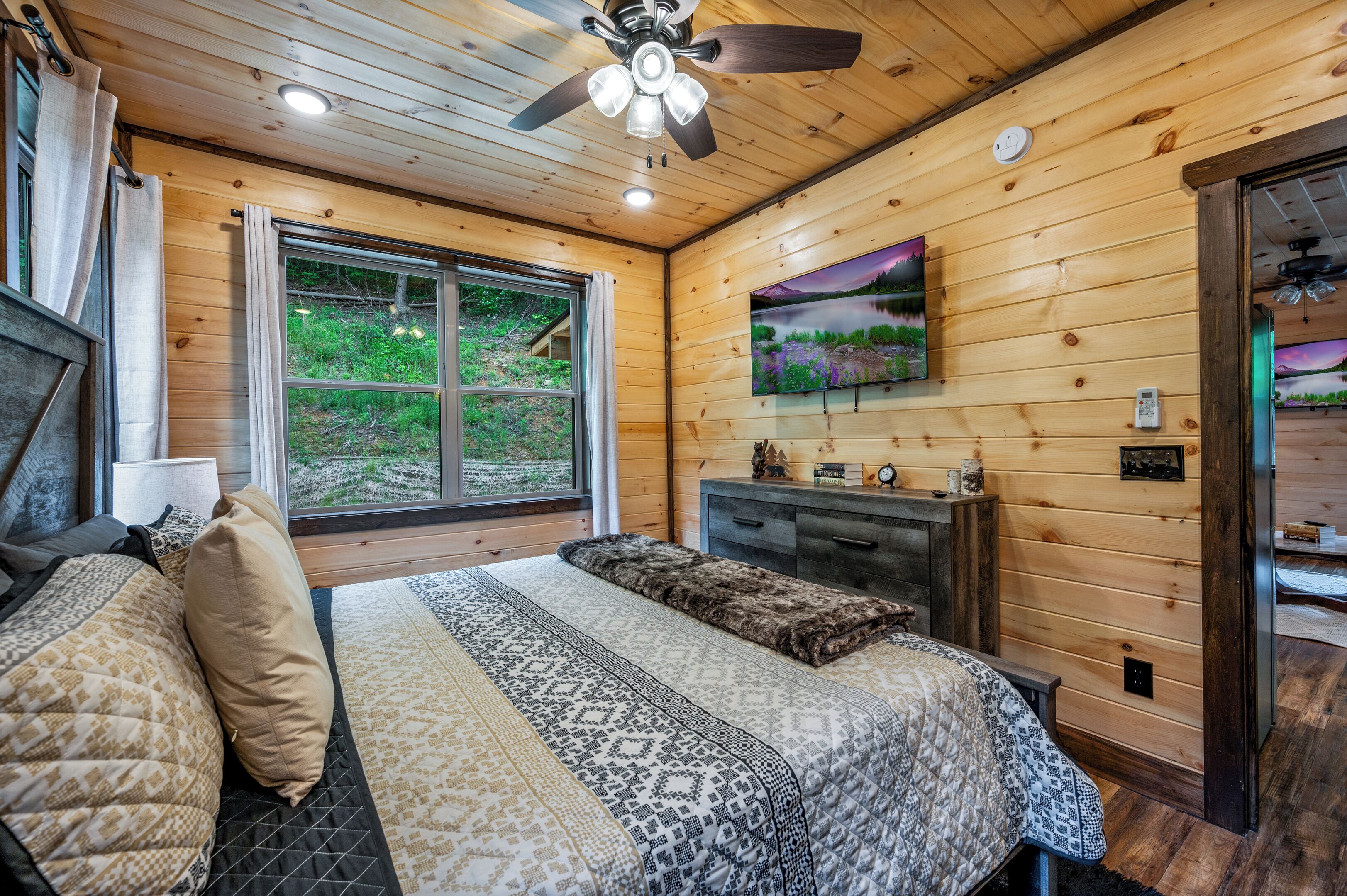 A wooden cabin bedroom with a bed, a dresser, a window, and a ceiling fan.