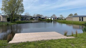 A lakeside view of a row of modern mobile homes with a wooden dock extending into the water. - Modern Chalet With 2 Bathrooms (West-Graftdijk)