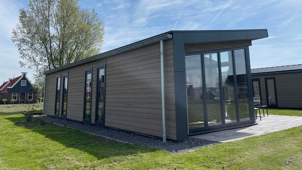 A modern building with a flat roof, large glass windows, and a wooden exterior. - Modern Chalet With 2 Bathrooms (West-Graftdijk)