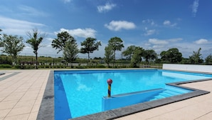 A rectangular swimming pool with a blue border, surrounded by a tiled deck, trees, and a fence in the background. - Modern Chalet With 2 Bathrooms (West-Graftdijk)