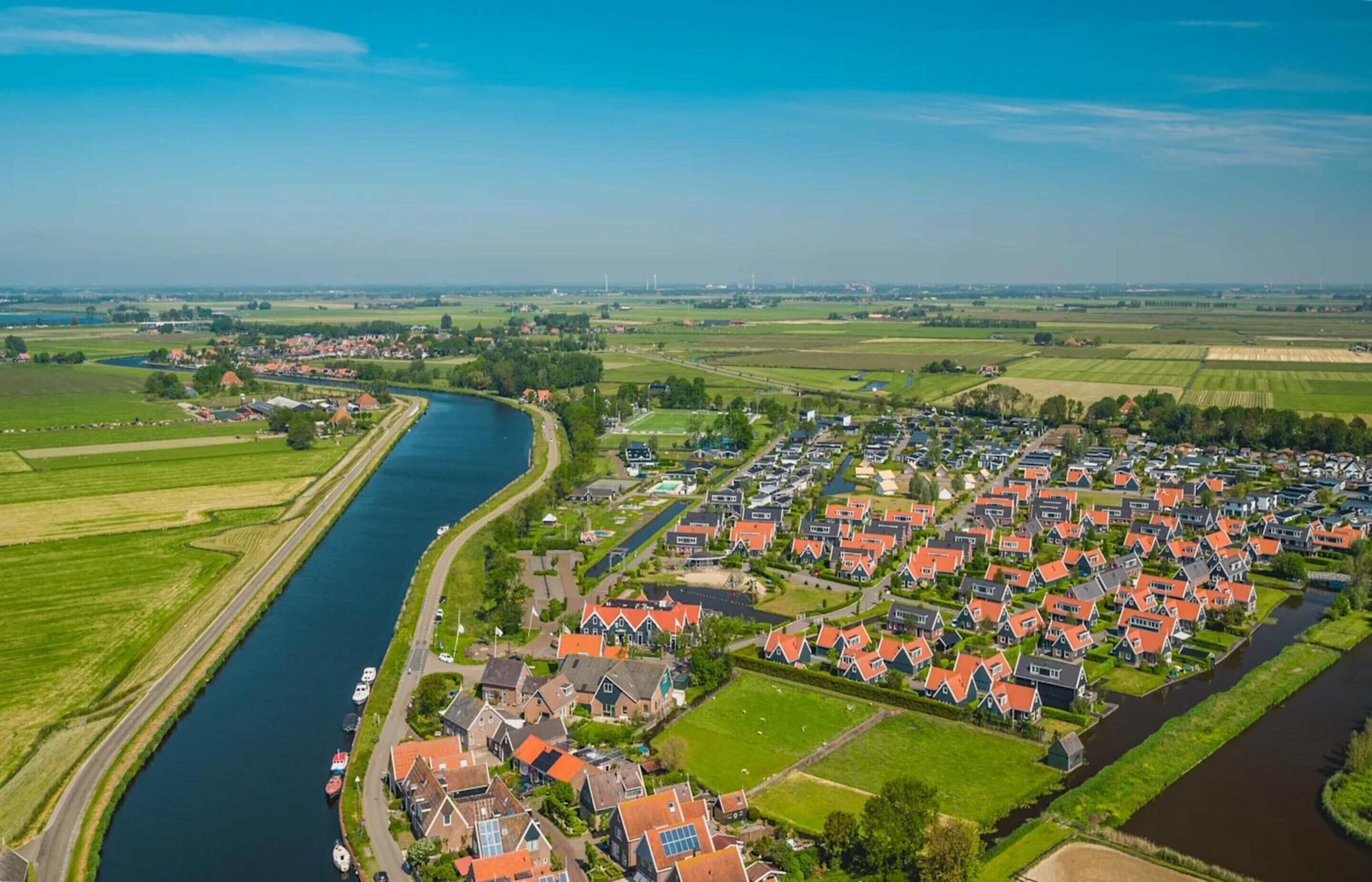 Ein Flussdorf mit traditionellen Häusern, einem Kanal und umliegenden Feldern.
