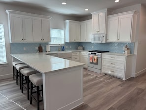 A kitchen with white cabinets, a central island with bar stools, a stove, and a microwave. - The Disco Cowgirl! 1 mile to Baylor, 1/2 mile to Magnolia Silos! (Waco)