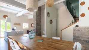 Un vaste espace dédié à la salle à manger, avec une table en bois, des chaises blanches et un mur en pierre.