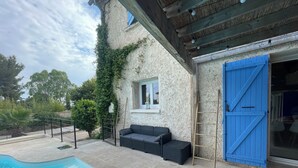 Un espace aménagé au bord de la piscine, avec une terrasse en pierre, un canapé noir et une porte bleue.