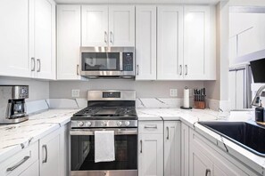 A modern kitchen with white cabinets, a stainless steel stove, a microwave, and a coffee maker. - Carlsbad Coastal Escape Walk To Beach• Legoland (Carlsbad)