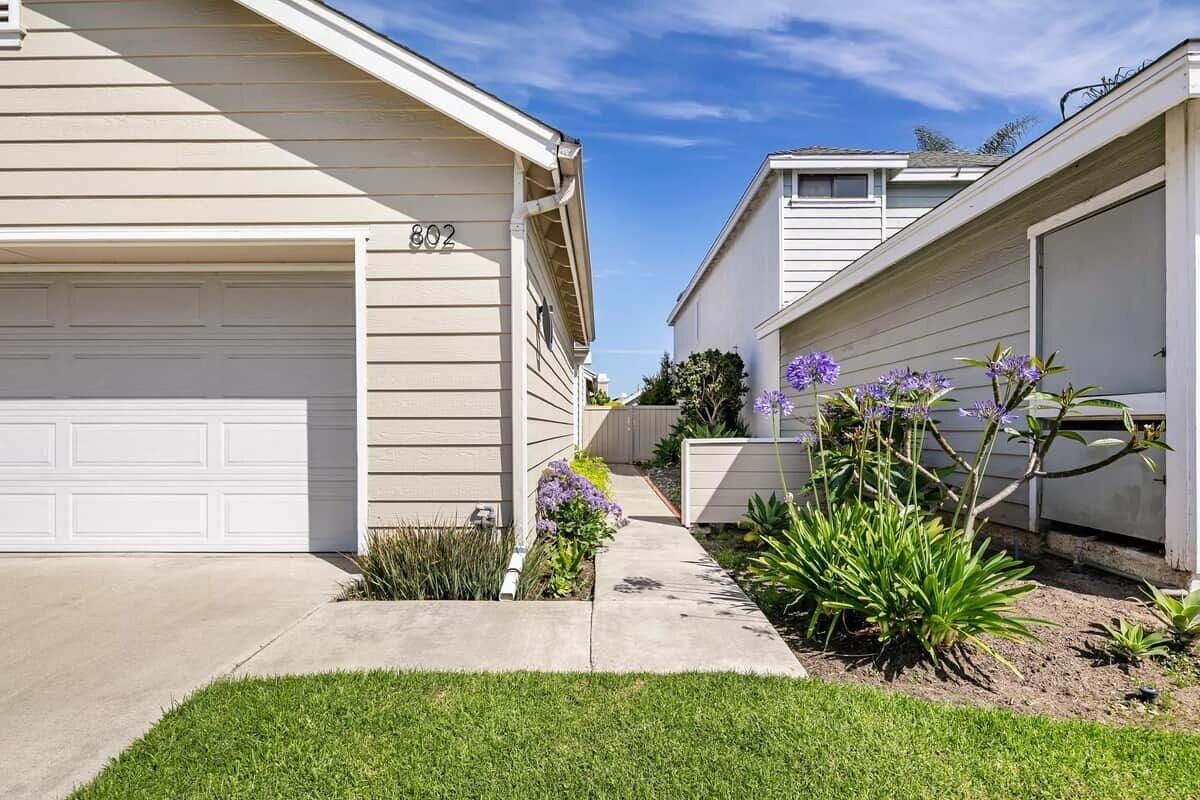 A residential building with a garage, number 802, and a well-maintained lawn with purple flowers.