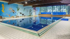 Piscina interior con un mural de vida marina, bancos de madera y ventanas grandes.