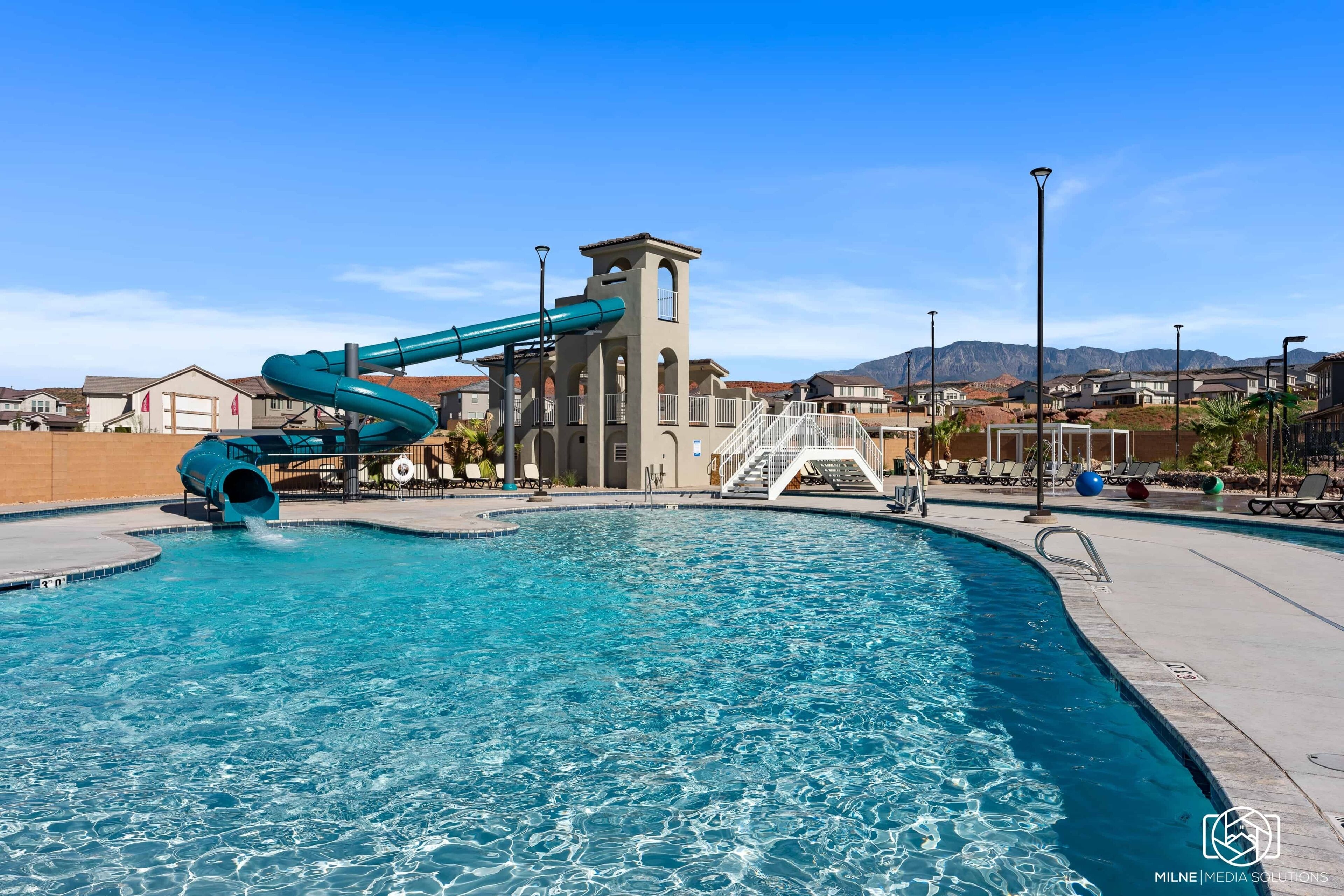 A swimming pool with a water slide, a tower, and a view of houses and mountains in the background.
