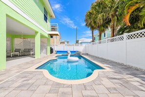 A swimming pool with a swan float, surrounded by a white fence, with a covered seating area and palm trees in the background. - 140 Pearl Paradise 3br/2ba W/ Pool! 3 Bedroom Home (Fort Myers Beach)