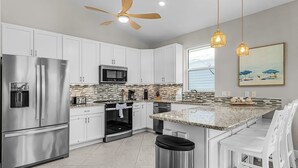 Una cocina moderna con armarios blancos, electrodomésticos de acero inoxidable, encimera de granito e iluminación colgante.