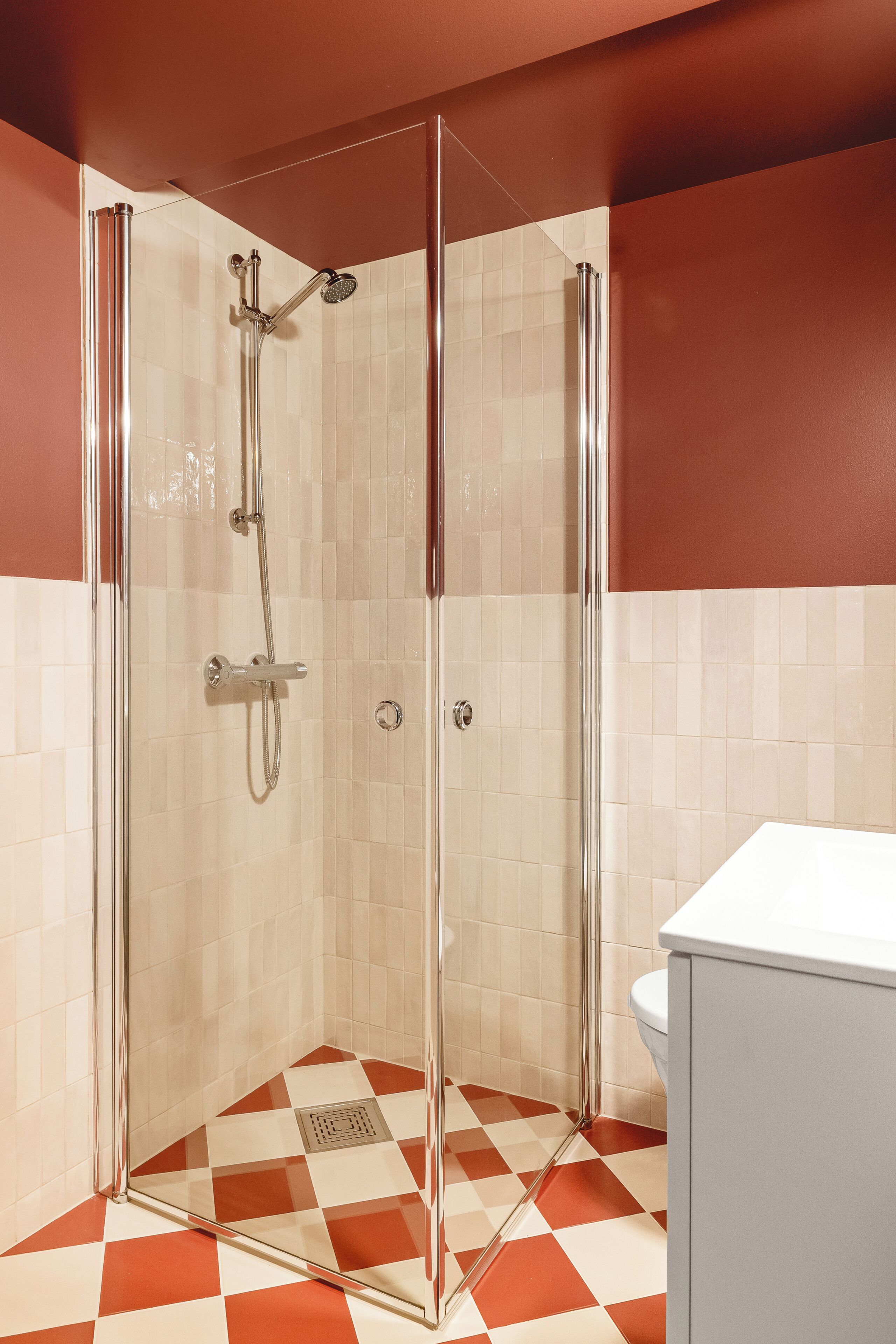 A shower with a glass door, a white tiled wall, and a checkered floor.