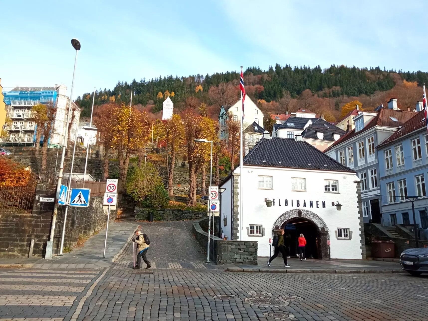 Une rue pavée avec un passage piéton, un bâtiment blanc portant l’inscription « FLOIBANE » et un mât avec des drapeaux.