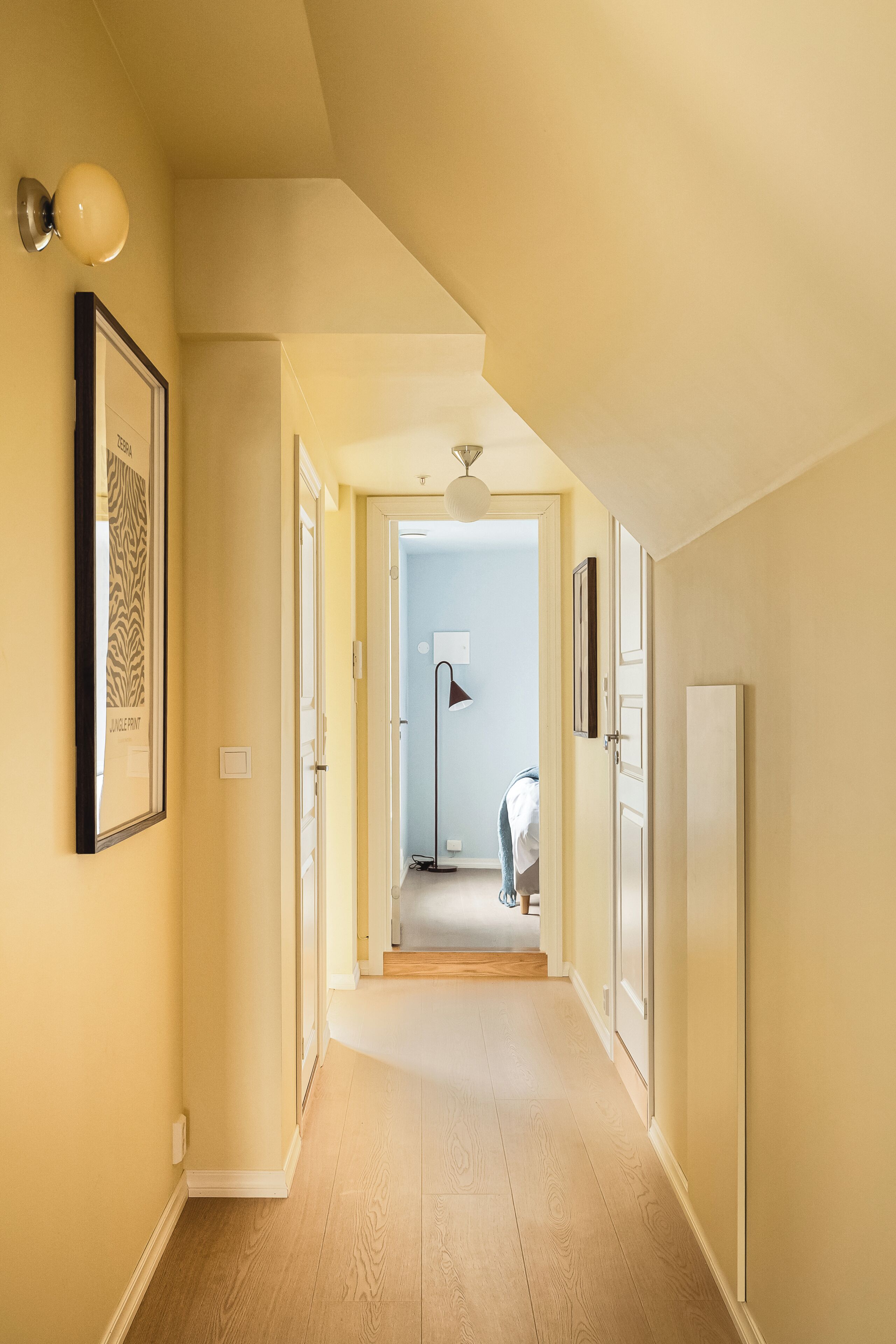 Un pasillo con ventilador de techo, cuadros enmarcados y una puerta que da a otra habitación.