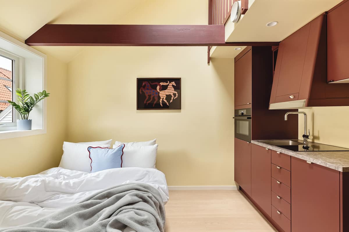 A bedroom with a bed, a bedside plant, and a window.