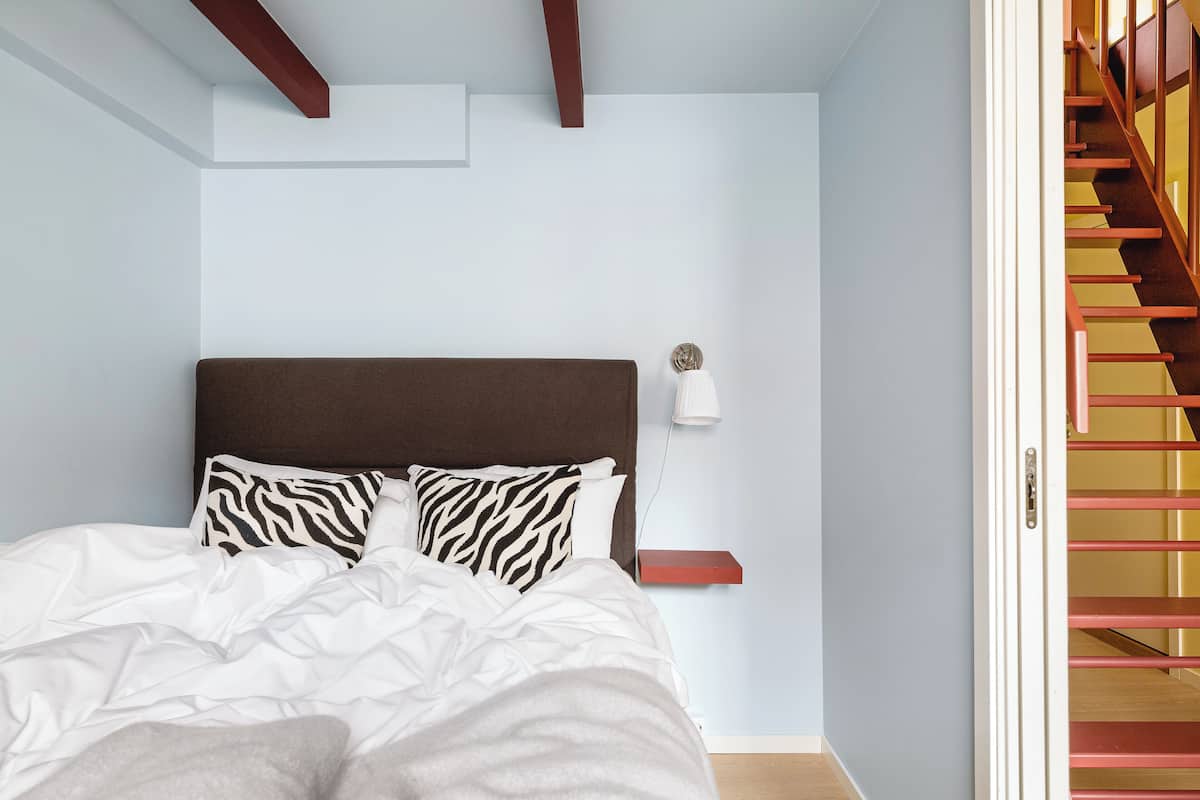 A bedroom with a bed, a nightstand, a wall-mounted lamp, and a staircase.
