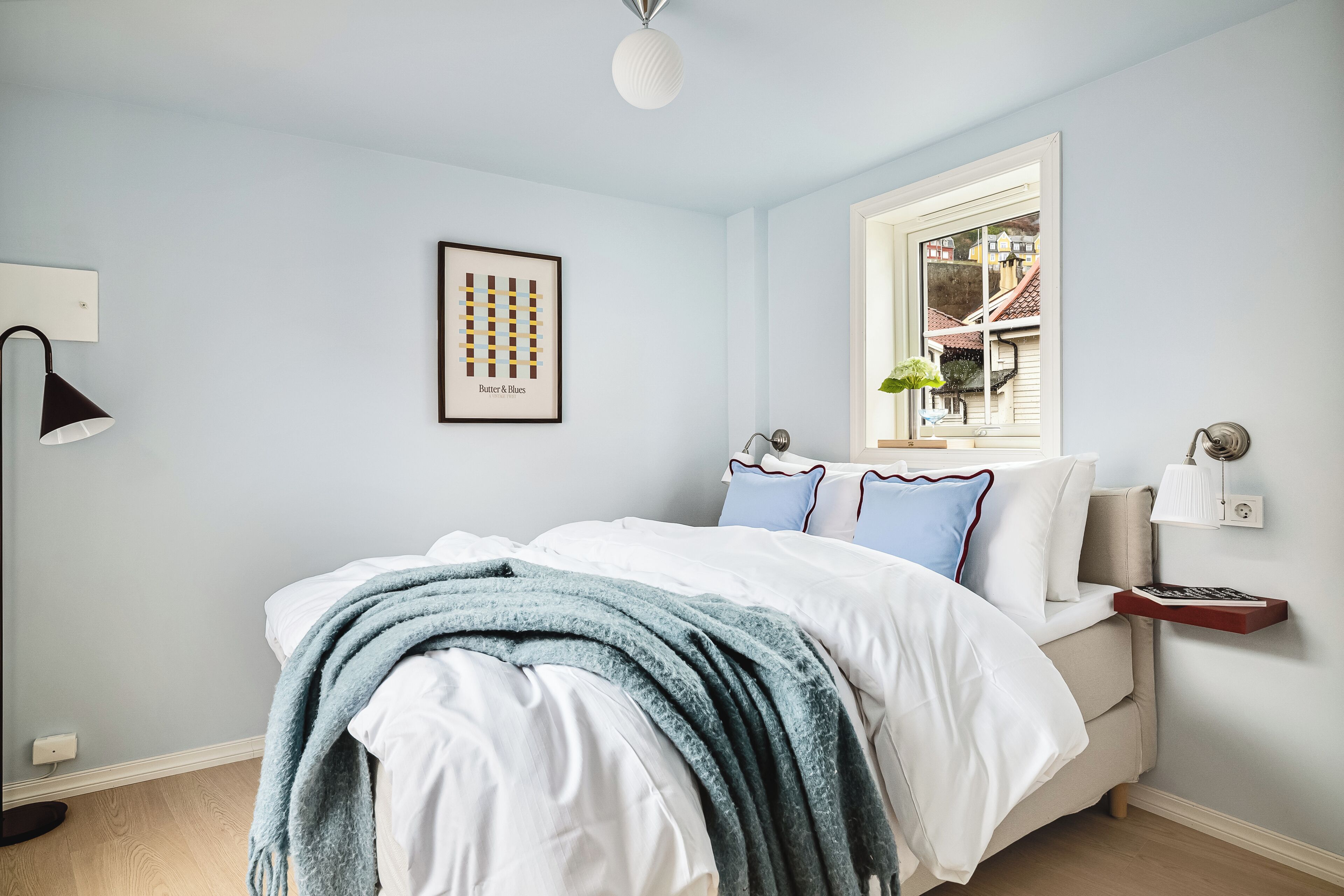 Un dormitorio con cama, ventana, mesita de noche y lámpara.