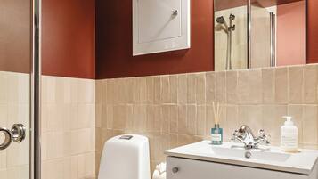 A bathroom with a toilet, sink, mirror, and shower.
