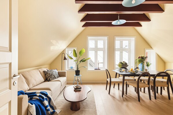 A cozy living room with a sofa, coffee table, dining table with chairs, and a potted plant.