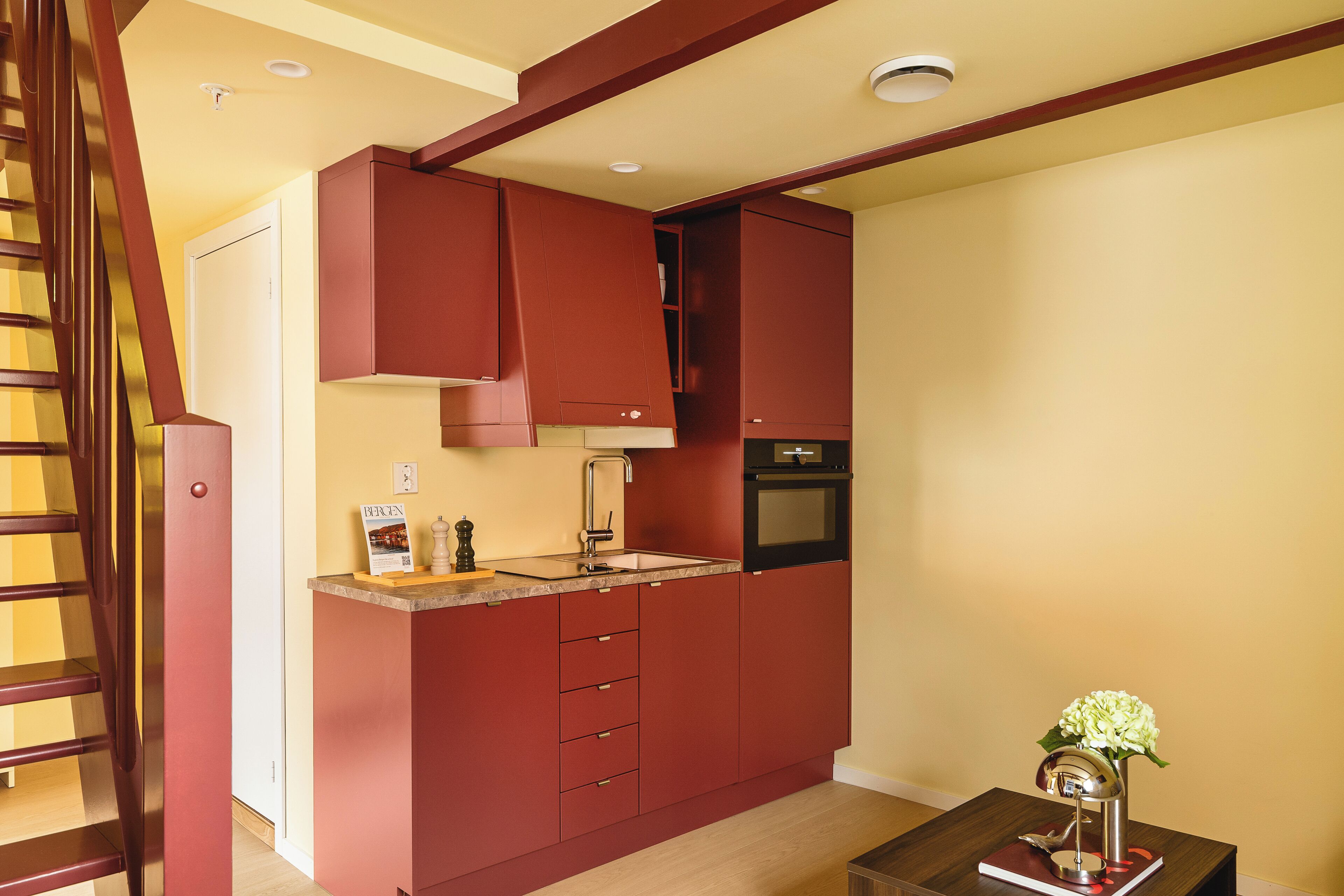 A modern kitchen with red cabinetry, a built-in oven, and a small table with a vase.