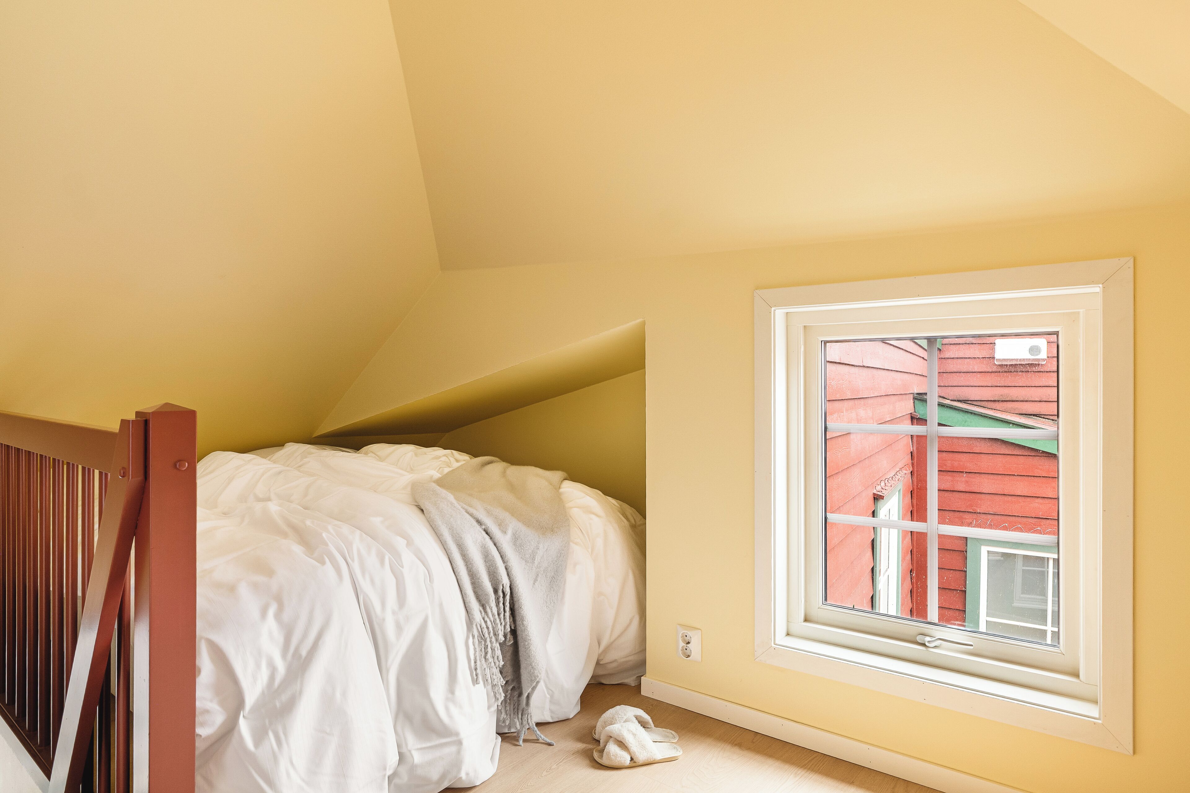Ein Schlafzimmer mit einem Bett, einem Fenster und Blick auf ein rotes Gebäude.