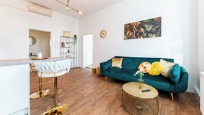 A modern living room with a teal sofa, a round coffee table, and a bar area with a white stool. - Vita Aurum Elbe-Apartments Neustadt  (Dresden)