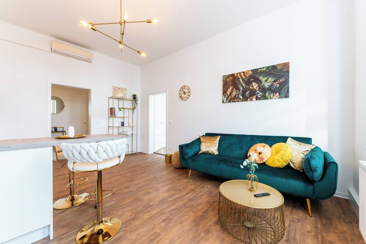 A modern living room with a teal sofa, a round coffee table, and a bar area with a white stool.